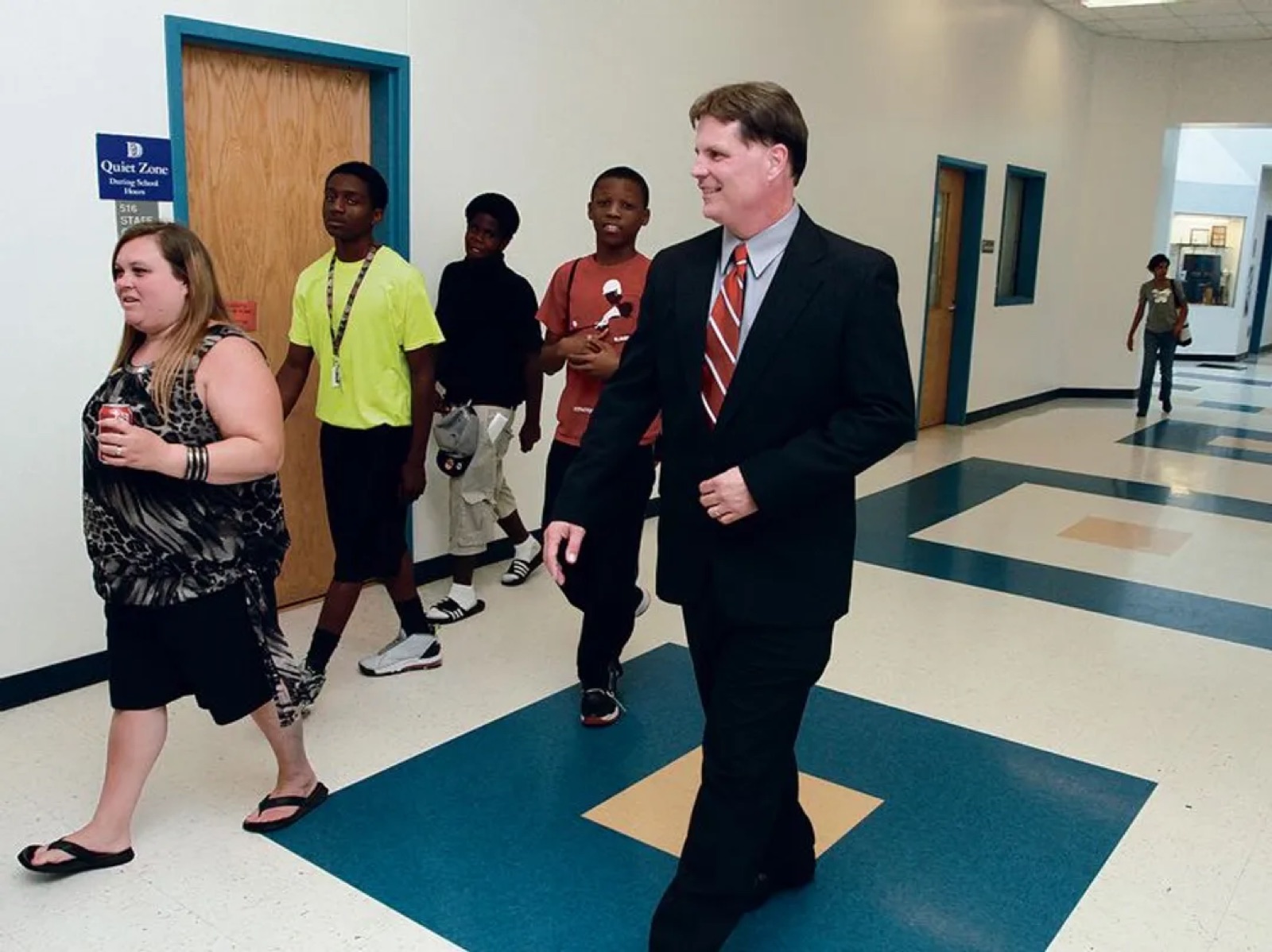 F.T. Franks walks a school hallway alongside a group of students, mid-stride and smiling.