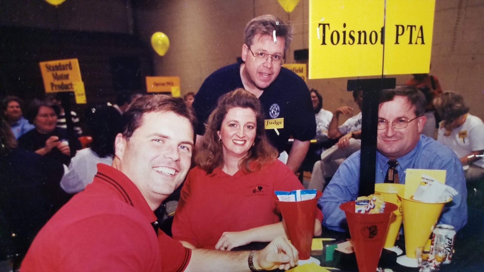 A younger F.T. Franks seated with three colleagues at a Toisnot PTA table at a community event.
